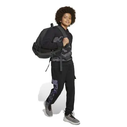 Παιδί που φοράει παιδικό φούτερ με κουκούλα Adidas Essentials Camo Fleece μαύρο, συνδυασμένο με μαύρο παντελόνι και σακίδιο.