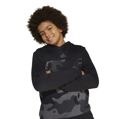 Παιδί που ποζάρει με παιδικό φούτερ με κουκούλα Adidas Essentials Camo Fleece μαύρο, με σταυρωμένα χέρια.